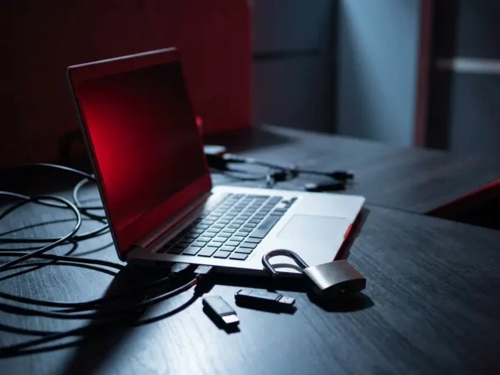 Laptop op kantoorbureau met rood schermgloed, open hangslot en verspreide USB-sticks, symboliseert een datalek of cyberaanval.
