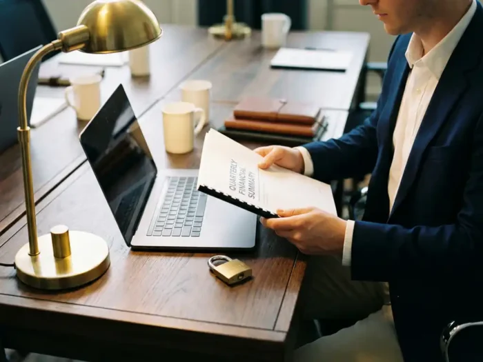Ondernemer bestudeert financieel rapport aan bureau met laptop en hangslot, warme amberkleurige bureaulamp verlicht werkplek.